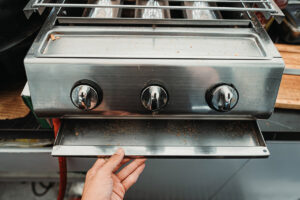 Znečištěné ovládací knoflíky a madlo zahradního grilu se zbytky mastnoty a jídla.
