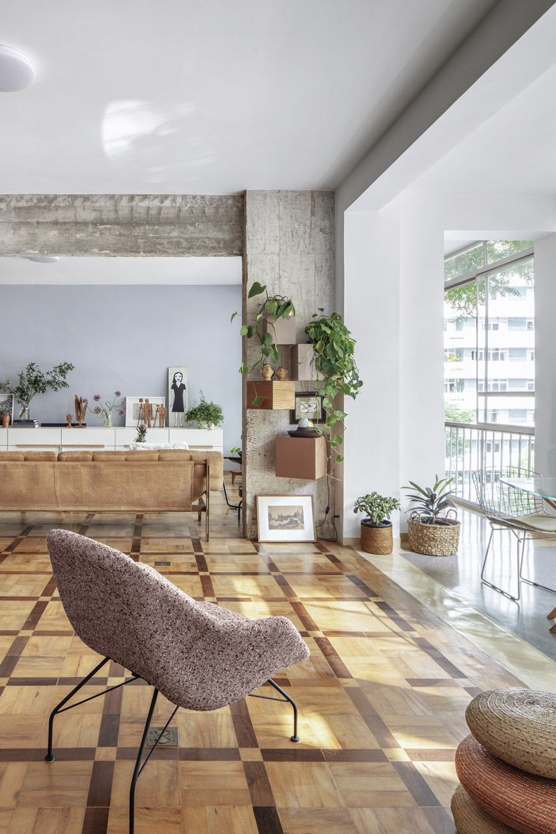 Denní zóna penthousu s přiznaným betonem, původní geometrickou dřevěnou podlahou, rostlinami a současným designovým nábytkem.