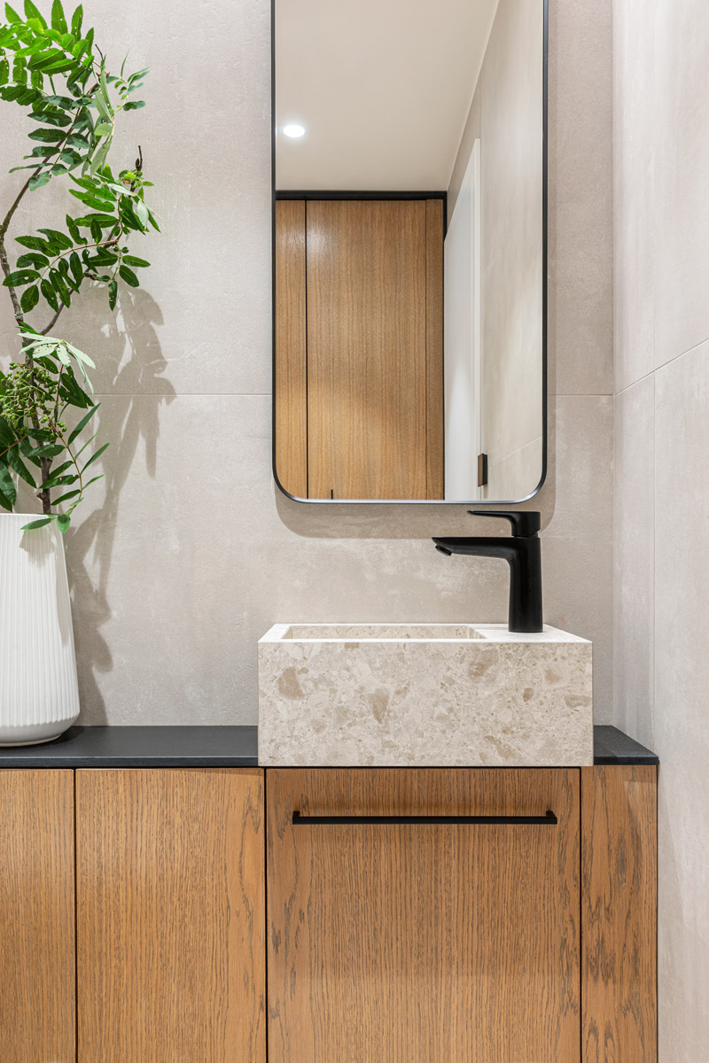 Kamenné umyvadlo, dubová skříňka a černá baterie vytvářejí elegantní kombinaci přírodních materiálů a moderních detailů.