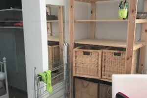 Původní interiér madridského minibytu před rekonstrukcí s otevřenými policemi a provizorními úložnými prostory.