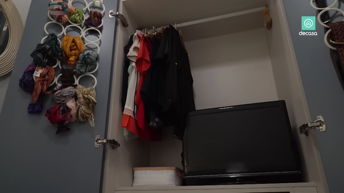 Otevřená šatní skříň s oblečením a televizorem ukrytým ve spodní části.