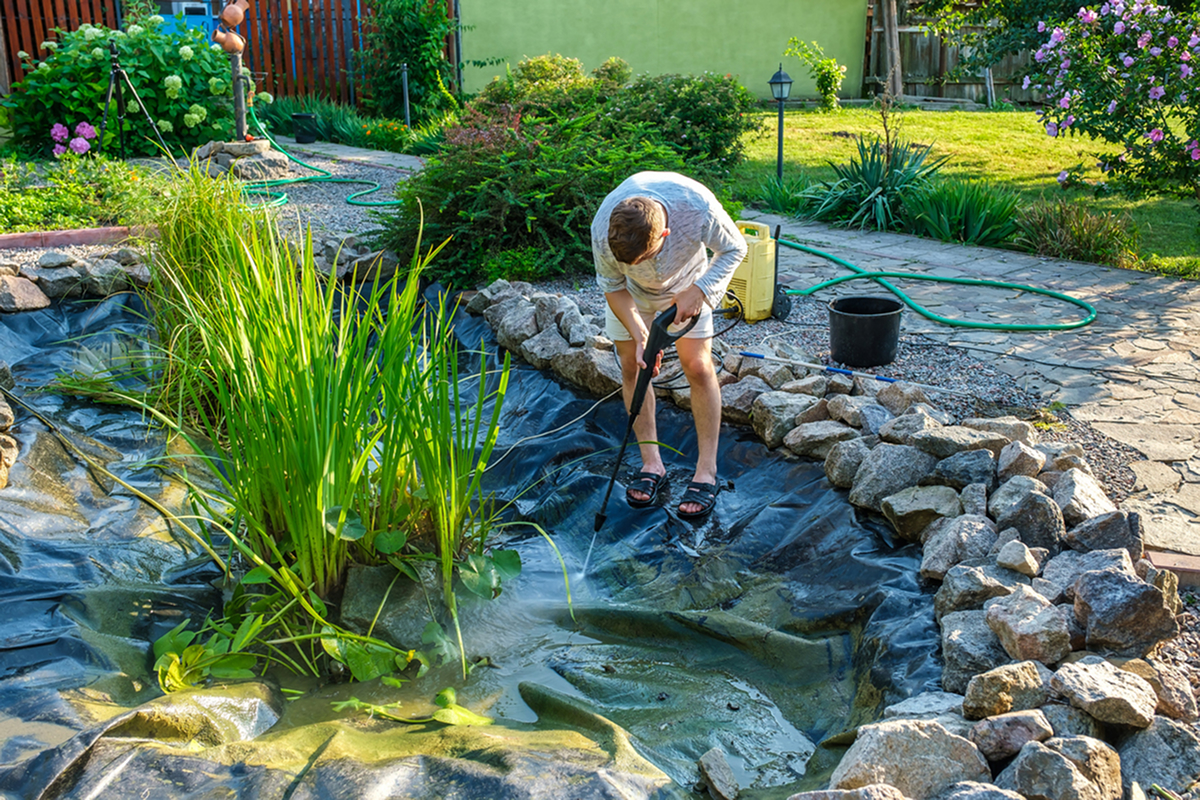 Čištění vypuštěného zahradního jezírka od kalu a usazenin pomocí proudu vody.