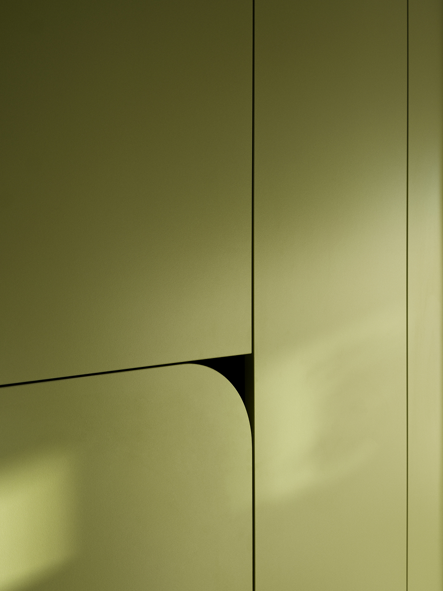 Detail bezúchytkových dvířek zelené vestavby se zaobleným rohem a čistými liniemi.
