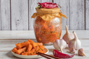 Pikantní dýňové kimchi s chilli a česnekem ve sklenici a na talíři.