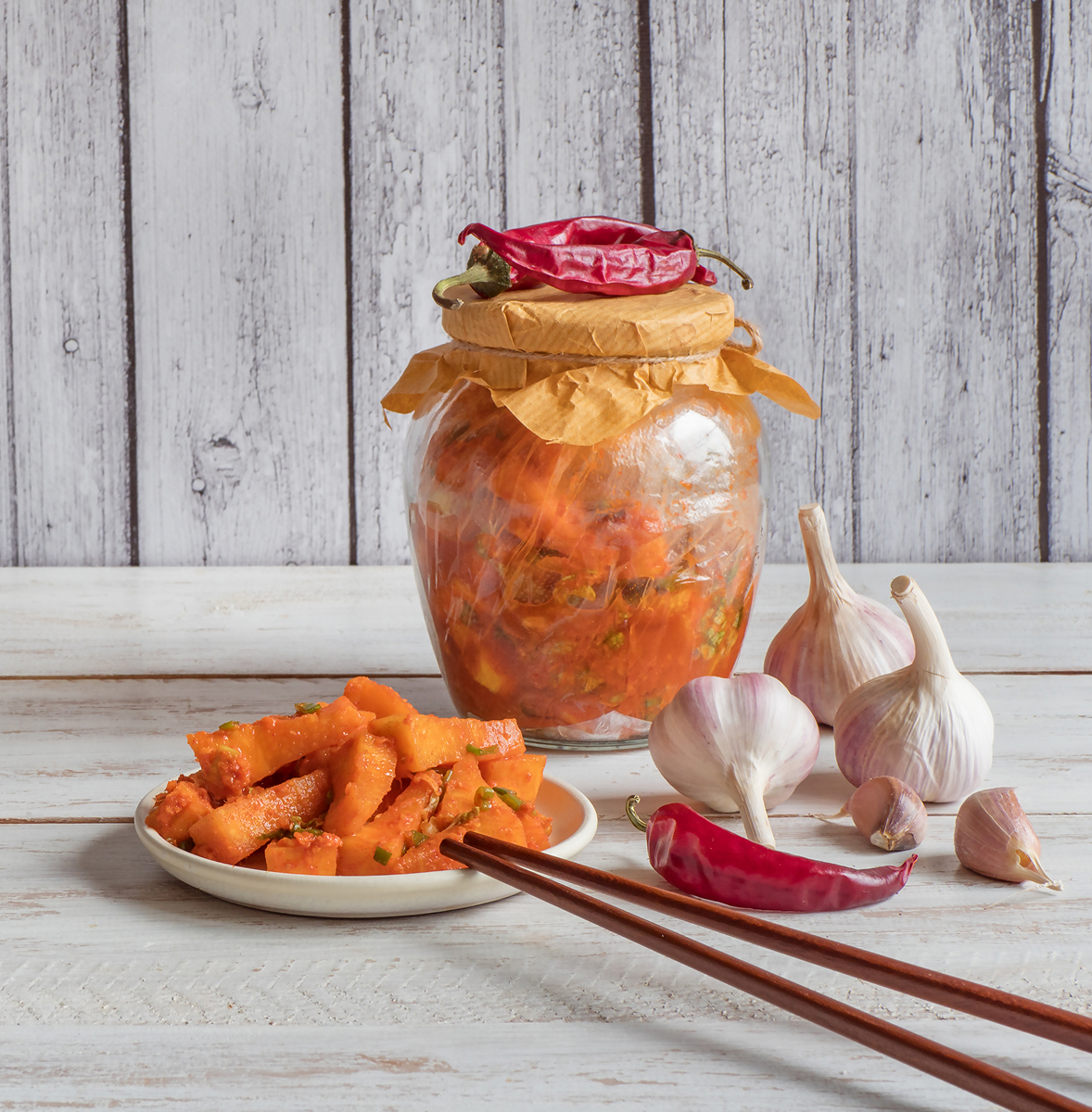Pikantní dýňové kimchi s chilli a česnekem ve sklenici a na talíři.