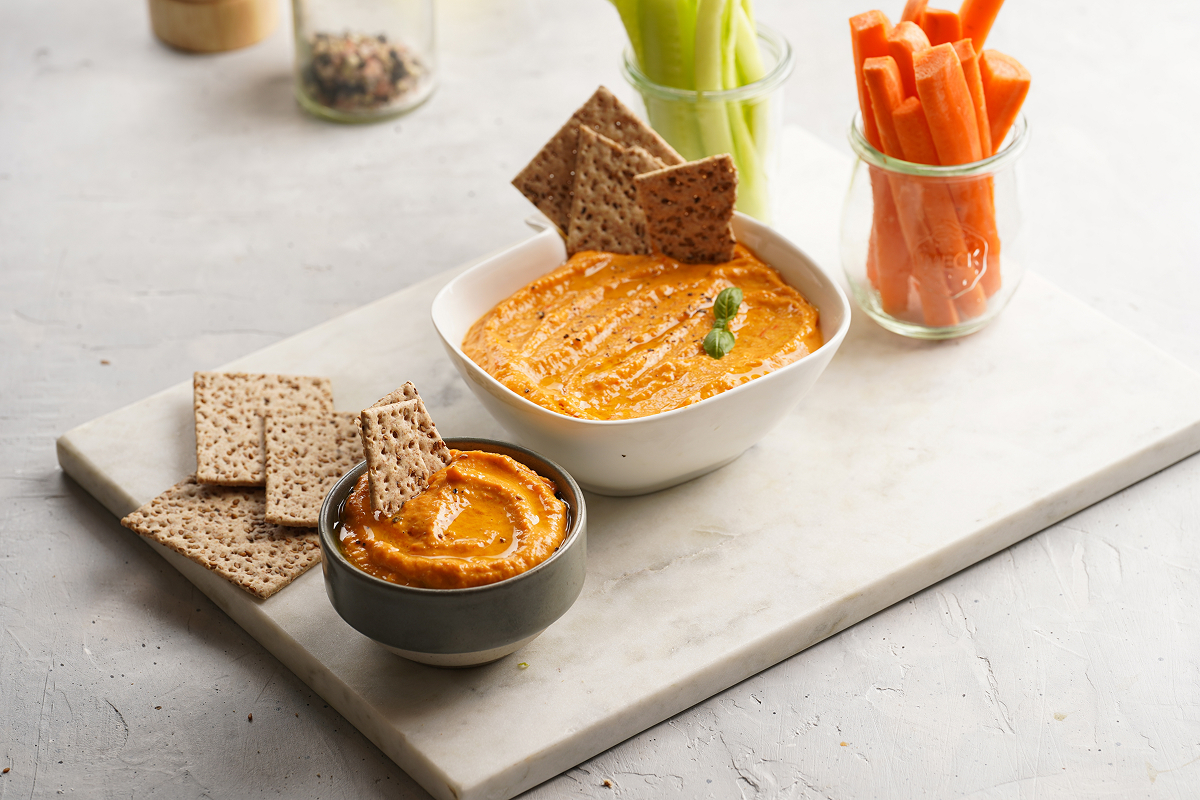 Krémový dýňový hummus podávaný se zeleninou a křupavými krekry.
