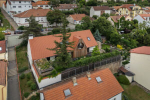Letecký pohled na dům s červenou střechou zasazený mezi původní zástavbu a zahrady.