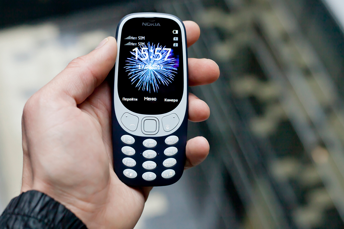 Klasický tlačítkový mobilní telefon držený v ruce.