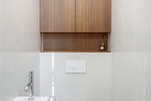 Malá toaleta se závěsným WC, hranatým umyvadlem a vestavnou skříňkou z tmavého dřeva.