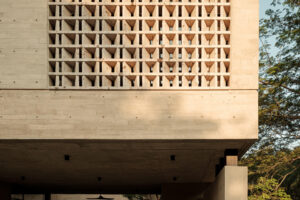 Detail světlé betonové fasády s geometrickou mříží z perforovaných tvárnic a zastřešeným prostorem v přízemí.
