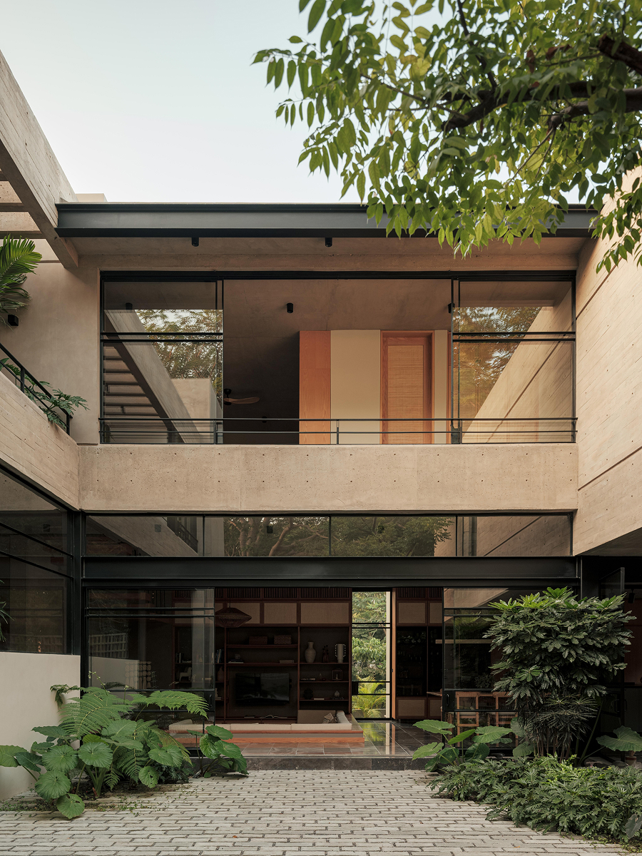 Moderní betonový dům Casa Akina s vysunutým horním podlažím, krytou terasou, velkým stromem a dlážděným nádvořím.