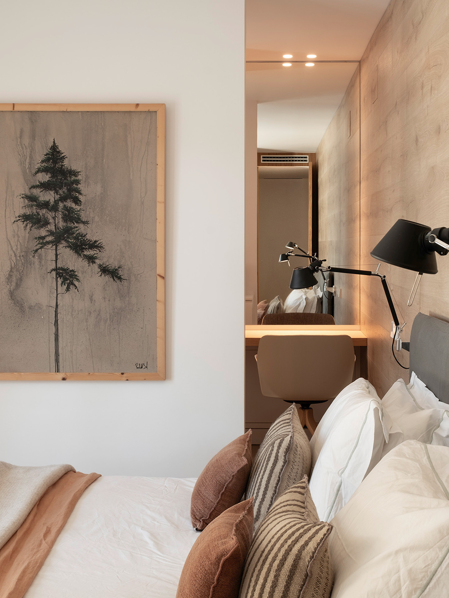 Detail ložnice s čalouněnou postelí, dřevěným obkladem, nástěnnými lampami a malým pracovním stolkem se zrcadlem.