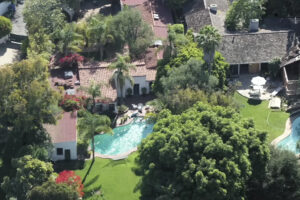 Letecký pohled na rozlehlé zahrady s bazény, vzrostlými stromy a domy s červenými taškovými střechami v losangeleské čtvrti Brentwood.