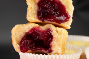 Rozkrojené muffiny se světlým těstem a výraznou červenou ovocnou náplní, která vytéká ze středu.